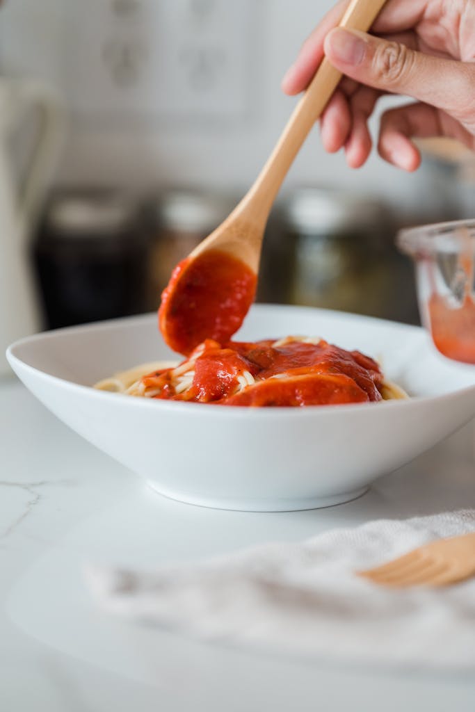 A hand serving delicious tomato sauce over pasta in a white bowl, perfect for an Italian cuisine concept.