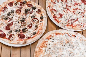 Close-up of three mouthwatering pizzas with mushrooms and pepperoni on a wooden table.