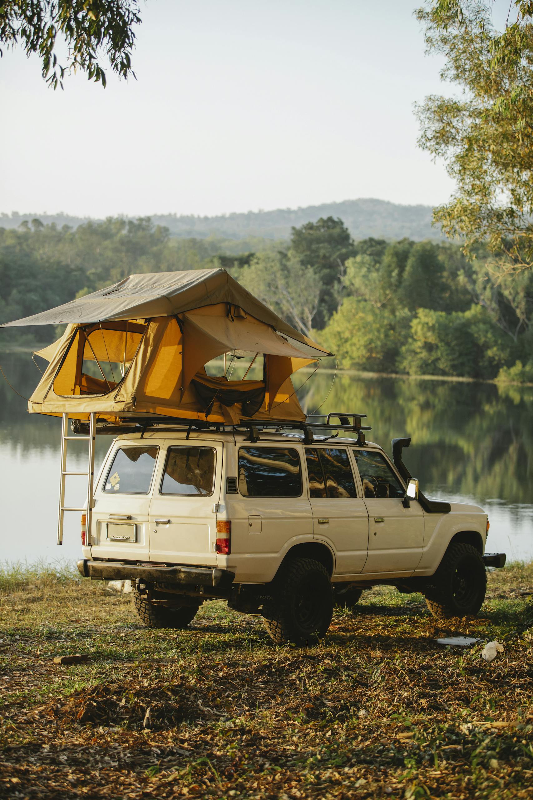 Explore the tranquil lakeside campsite with a car and rooftop tent, perfect for summer adventures.