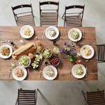 Top view of a wooden table set with pasta dishes, fresh ingredients, and drinks for a cozy meal.
