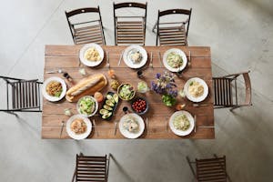 Top view of a wooden table set with pasta dishes, fresh ingredients, and drinks for a cozy meal.