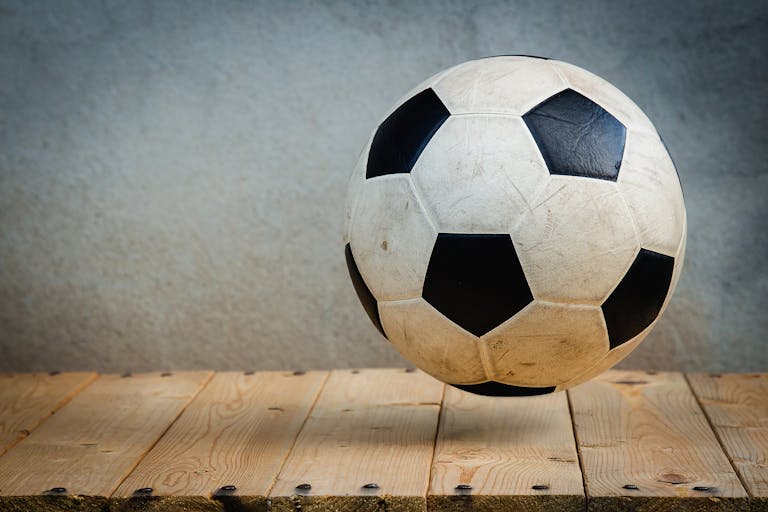 Vintage soccer ball resting on wooden planks against a textured background, symbolizing sports tradition.