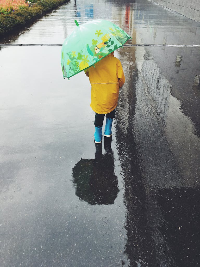 Photo by Anna Moreva Lapsi vesisateessa sateenvarjon kanssa päällään keltainen sadetakki